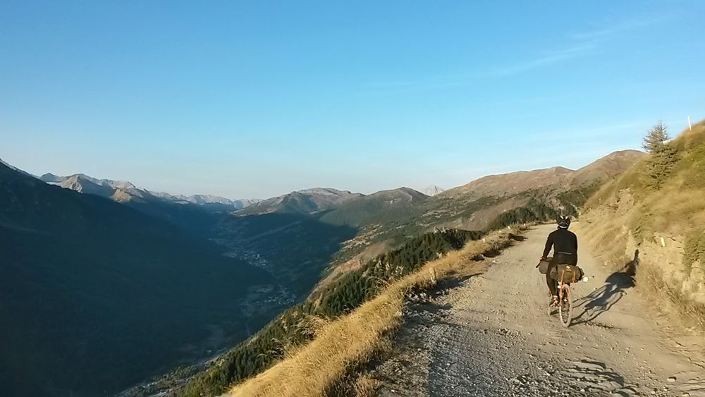 a view across a valley, with a cyclist on a track, roughly following their shadow
